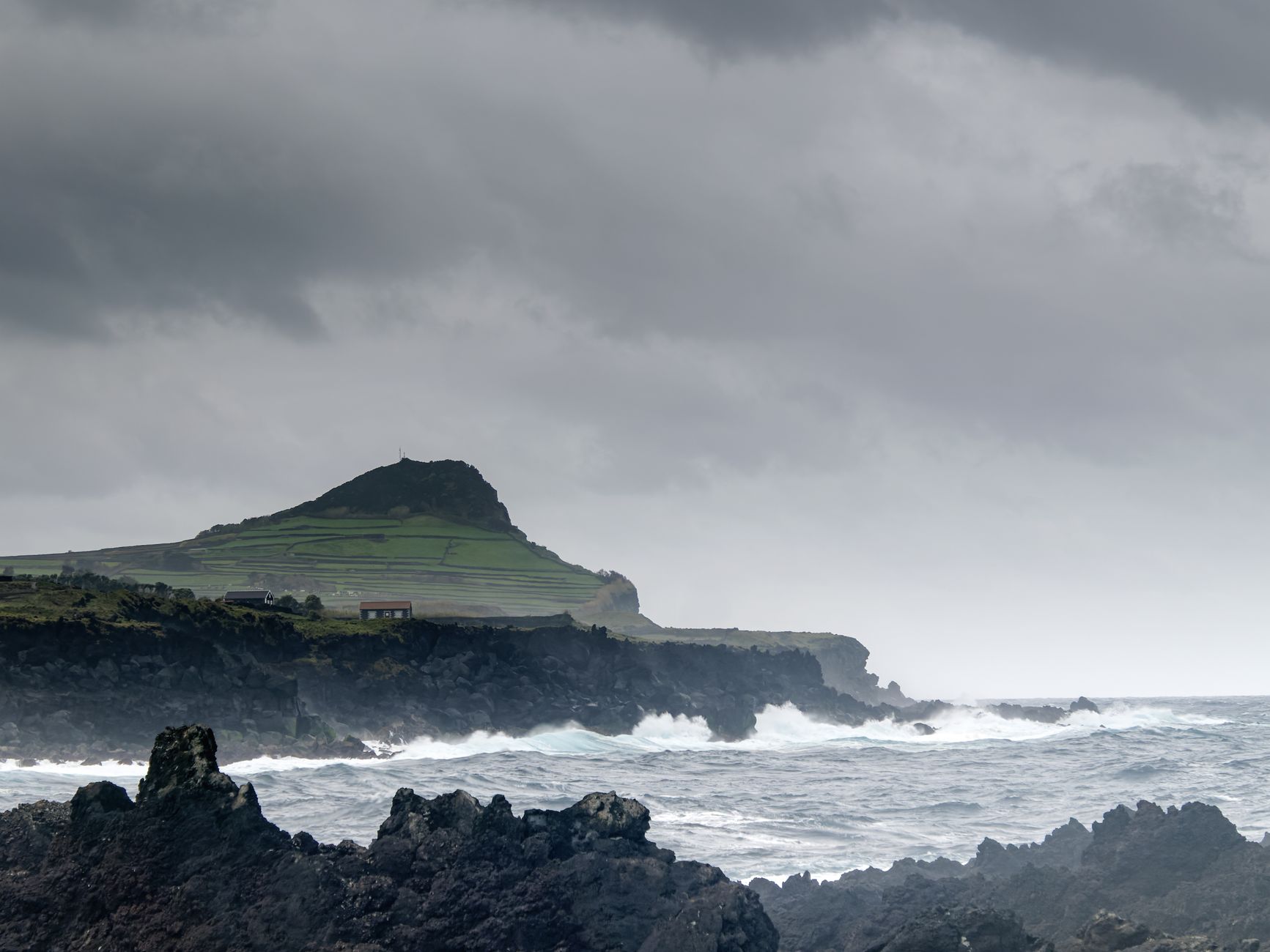 Aguaceiro a passar sobre uma costa vulcânica nos Açores com um arco-íris sobre o mar