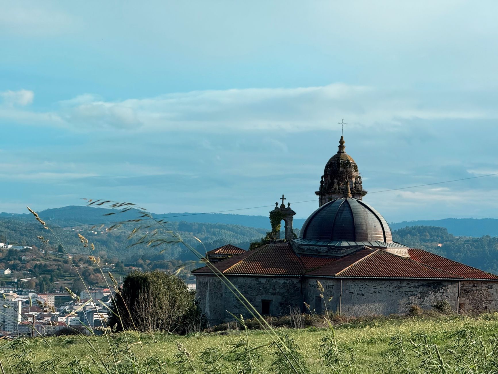 Rua tranquila de uma aldeia açoriana com hortênsias, uma igreja de pedra e nuvens baixas sobre as colinas